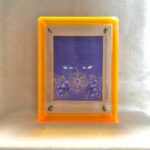 Front view of purple Vairochana Buddha Eyes print in a yellow floating translucent acrylic frame.