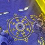 Close-up of original hand-painted gold linework and wisdom Buddha eyes on purple canvas.