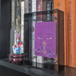 Purple Vajrasattva Buddha Eyes Thangka in a grey translucent acrylic frame styled on a bookshelf.