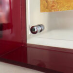 Close-up of corner magnetic screw on red translucent acrylic display frame.