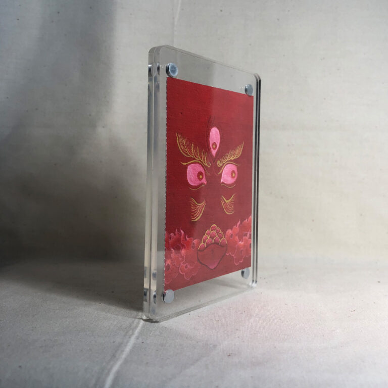 Side-angle view of freestanding clear acrylic block displaying Red Jambhala line art.