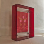 Side perspective of red Jambhala Buddha Eyes art inside a red translucent acrylic frame.
