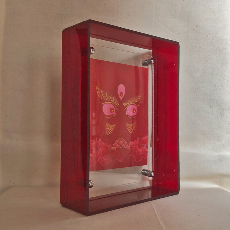 Side perspective of red Jambhala Buddha Eyes art inside a red translucent acrylic frame.