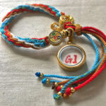 Backside view of the orange Shakyamuni charm bracelet displaying the authentic brand emblem.