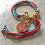 Flatlay layout of the orange Shakyamuni Buddha Eyes braided cord bracelet for mindfulness.