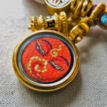 Close-up of Shakyamuni Buddha Eyes orange charm with hand-painted gold linework.