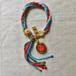 Full view of orange Shakyamuni Buddha Eyes pendant and braided cord.