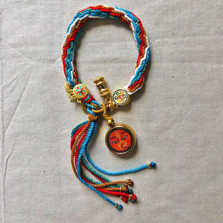 Full view of orange Shakyamuni Buddha Eyes pendant and braided cord.