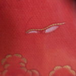Close-up of original hand-painted gold cloud linework and wisdom eyes on orange canvas texture.