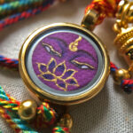 Close-up of Vajrasattva purple Buddha Eyes charm with hand-painted gold linework.