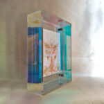 Side perspective of white Jambhala Buddha Eyes art inside an iridescent translucent acrylic frame.