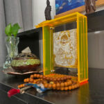 White Jambhala Thangka yellow acrylic art block styled next to prayer beads on a desk.