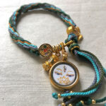 Top-down close-up of White Tara Buddha Eyes pendant and braided tassel end.