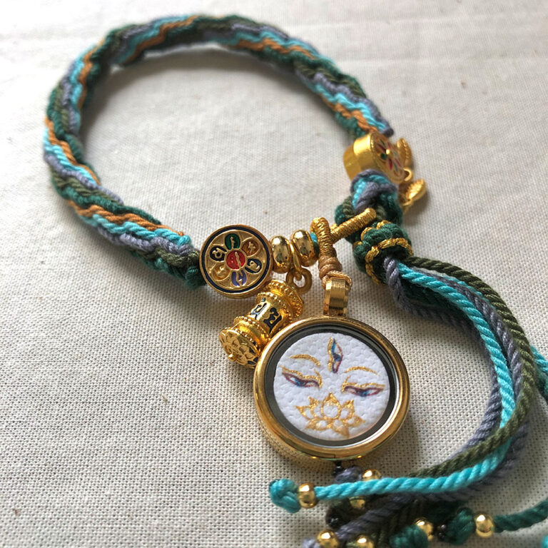 Top-down close-up of White Tara Buddha Eyes pendant and braided tassel end.