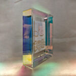 Side perspective of white Tara Buddha Eyes art inside an iridescent translucent acrylic frame.