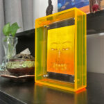 Yellow Manjushri Buddha Eyes Thangka in a yellow translucent acrylic frame styled on a study desk.