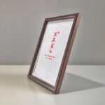 Side perspective view of A4 dark wood framed red calligraphy print on tabletop