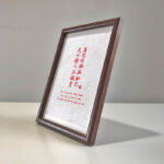 Side perspective view of A4 dark wood framed red farewell calligraphy print on tabletop