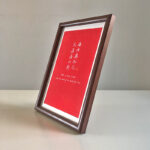 Side perspective view of A4 dark wood framed red friendship calligraphy print on tabletop