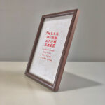 Side perspective view of A4 dark wood framed red wedding calligraphy print on tabletop
