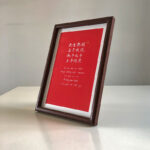 Side perspective view of A4 dark wood framed red love vows calligraphy print on tabletop
