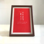 Frontal view of A4 red paper Chinese calligraphy print in dark wood frame on clean tabletop