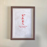 Frontal view of A4 red Chinese calligraphy print in dark wood frame on clean desk. Warm home blessing desk display for living rooms and entryways.