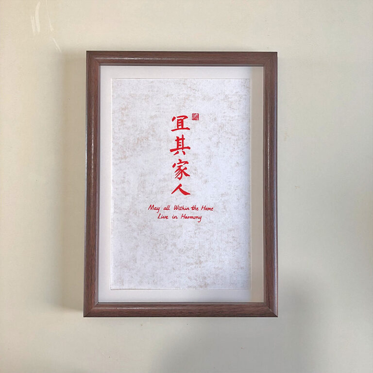 Frontal view of A4 red Chinese calligraphy print in dark wood frame on clean desk. Warm home blessing desk display for living rooms and entryways.