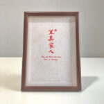 Frontal view of A4 red paper Chinese calligraphy print in dark wood frame on clean desk