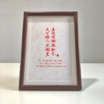 Frontal view of A4 red paper Chinese farewell calligraphy print in dark wood frame on clean desk
