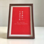 Frontal view of A4 red paper Chinese friendship calligraphy print in dark wood frame on clean desk