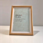Frontal view of A4 light green paper Chinese calligraphy print in natural wood frame on clean desk