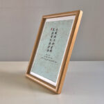Side perspective view of A4 wooden framed calligraphy print on tabletop