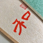 Macro close-up of handwritten red Chinese character Harmony He with red artist seal on cream Xuan paper.