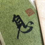 Extreme macro close-up of handwritten Chinese character Rest Xi with red artist seal on green textured Xuan paper.