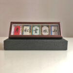 Handwritten 5-character calligraphy frame placed on a dark gift box display base.