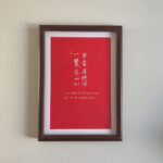 A4 framed red paper Chinese calligraphy art print with dark wood frame hanging on wall