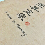 Close-up of Chinese calligraphy characters and English translation "A Home in Harmony" with red seal stamp