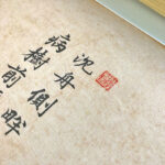 Close-up of Xingzhuo Chinese calligraphy brush strokes and red seal stamp on warm textured fine art paper