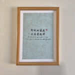 A4 framed Chinese calligraphy art print with natural wood frame hanging on wall