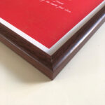 Macro detail of smooth dark walnut wood frame corner for A4 red art display