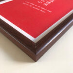 Macro detail of smooth dark walnut wood frame corner for A4 red art display