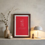 Framed red Chinese calligraphy art print set on a minimalist wooden sideboard with modern ceramic vases and a warm table lamp.