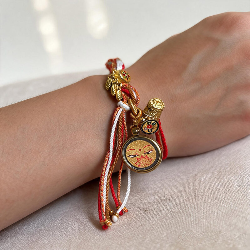 Gold Shakyamuni Buddha Eye pendant bracelet worn on wrist with cream woven cord.