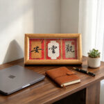 Red Song Brocade calligraphy display Guan Yun An on a dark wooden office desk beside a laptop and leather notebook.