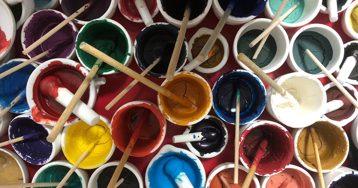 Top view of vibrant natural mineral pigment bowls and brushes used in traditional Thangka painting.