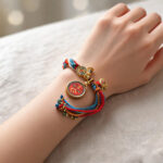 Orange Chenrezig Buddha Eye pendant bracelet on wrist with colorful cord trim.
