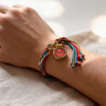 Red Amitayus Buddha Eye circular pendant bracelet on wrist with red braided cord.