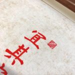 Close-up of red Xingzhuo Chinese calligraphy brush strokes and red seal stamp on textured paper