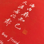 Close-up of white Xingzhuo Chinese friendship calligraphy characters and gold seal stamp on red paper